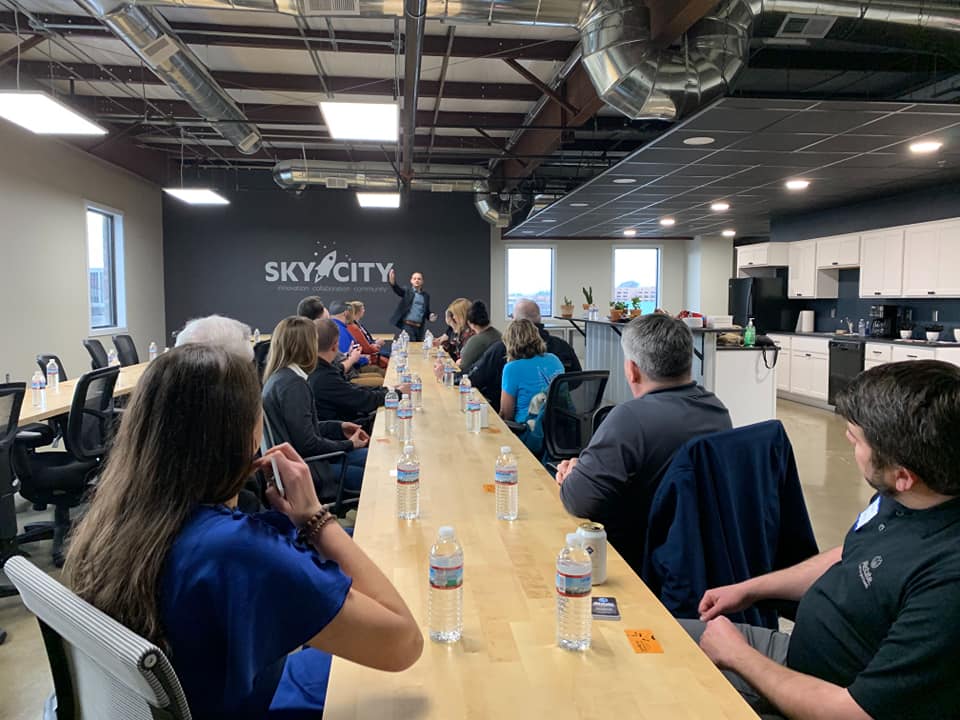 Image of a Sky City event with attendees sitting at a long conference table listening to the speaker